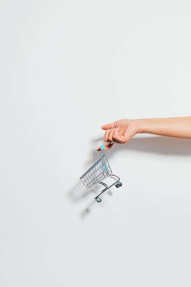 A miniature shopping cart being lifted by a person's hand